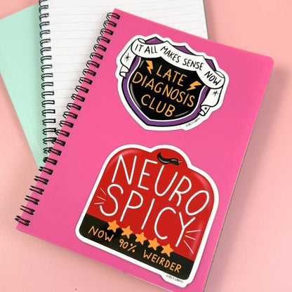 Pink notebook with 'Late Diagnosis Club' and 'Neuro Spicy' stickers on a pink background